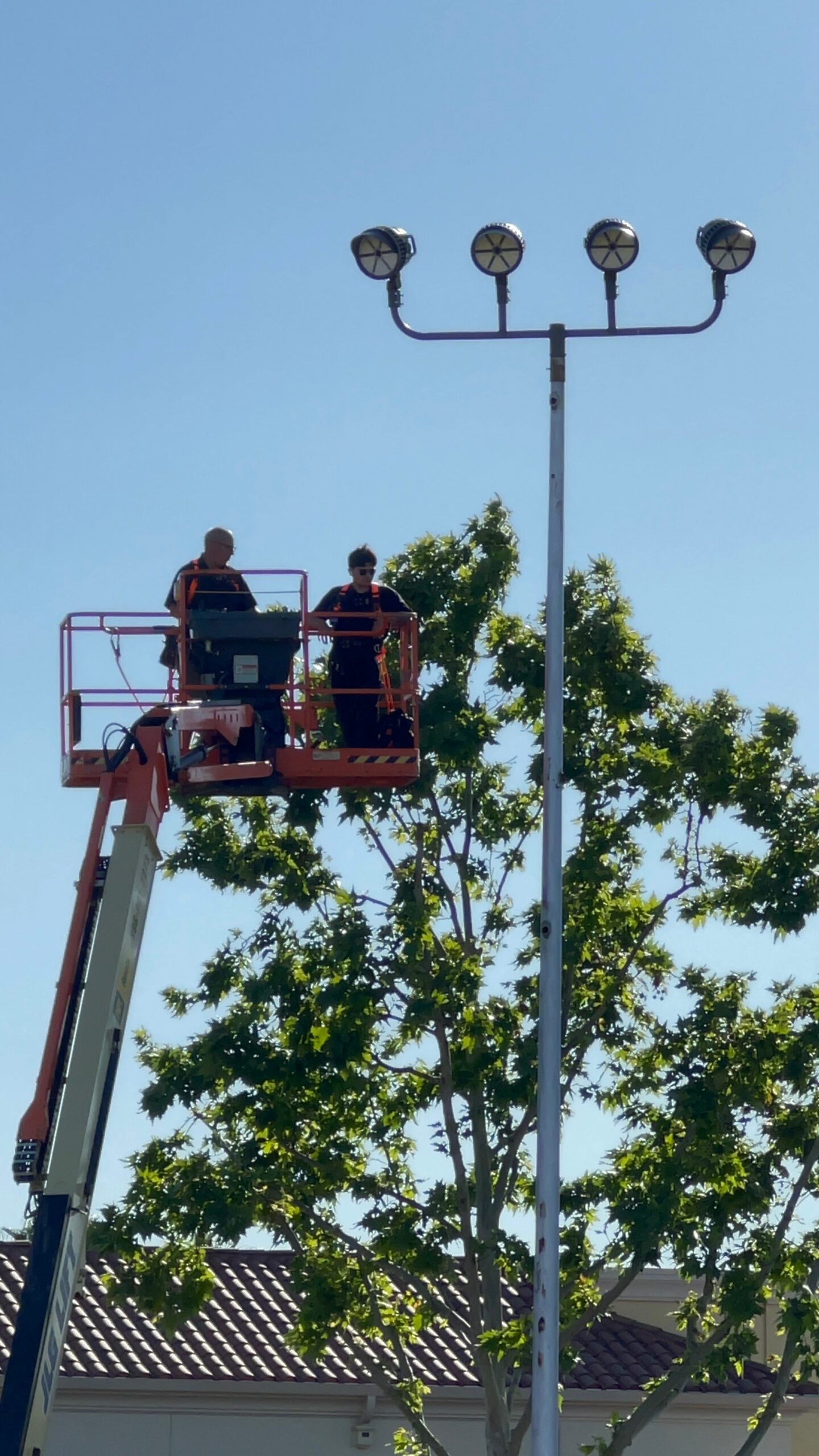 Two Reliant technicians in cherry picker at top of ball field light pole